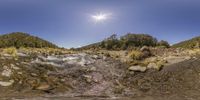 a creek with some rocks and water with sun in the background and the blue sky