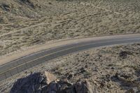 a motorcycle riding down a winding highway between hills and dry grass on a sunny day