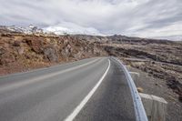 a car is going down the mountain road in the background of snow capped mountains and rocks