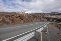 a mountain road with a winding asphalt road with a gravel road side and the snow covered mountain in the background