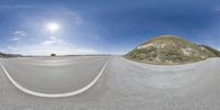 a fish eye lens view of a mountain road with an asphalt tarmac and the sun shining