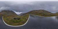 a couple of curved curves on a mountain road between mountains with clouds rolling in the background