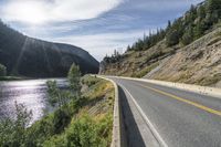 a car is driving down the road along the mountains near the river below and the bridge