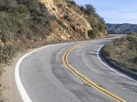 a curve road with trees, shrubs and rocks on both sides and one of the sides is slightly sloped