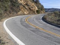 a curve road with trees, shrubs and rocks on both sides and one of the sides is slightly sloped