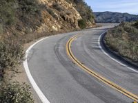 a curve road with trees, shrubs and rocks on both sides and one of the sides is slightly sloped