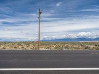 a telephone pole on the side of the road by the desert with mountains in the background