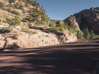 a person on a motorcycle riding down a mountain road in front of a cliff and pine trees