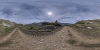 a wide angle panoramic view of a dirt road near a mountain with a sky background