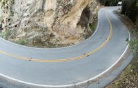 the curve in a mountain road that is painted grey and yellow with a green tree in the middle