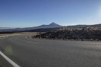 the curved road looks beautiful with mountains in the background and a blue sky on the side