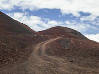 a dirt road with a hill behind it that is covered by dark rocks and dirt