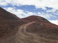 a dirt road with a hill behind it that is covered by dark rocks and dirt