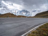 a person riding a bike down the road next to a mountain side with clouds in the sky