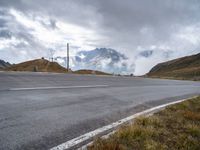 a person riding a bike down the road next to a mountain side with clouds in the sky