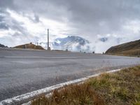 a person riding a bike down the road next to a mountain side with clouds in the sky