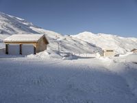 two wooden boats sit in the snow next to a small house, some are surrounded by thick, snow covered slopes