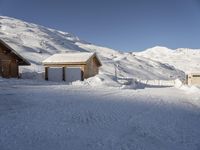 two wooden boats sit in the snow next to a small house, some are surrounded by thick, snow covered slopes