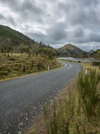 a long road with two lanes between mountains and trees in the distance are green grass