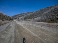 a person riding a motorcycle down a dirt road by a large hill covered with trees