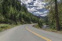 a scenic, mountain and tree - lined road on an island or land, with a yellow strip