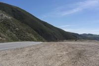 the side of the mountain road stretches into the distance, while a motor cycle is driving down it