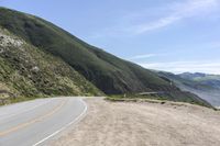 the side of the mountain road stretches into the distance, while a motor cycle is driving down it