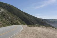 the side of the mountain road stretches into the distance, while a motor cycle is driving down it