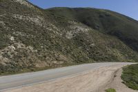 the side of the mountain road stretches into the distance, while a motor cycle is driving down it