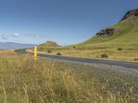 the road is next to the mountain with grass and wildflowers on the side