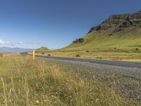 the road is next to the mountain with grass and wildflowers on the side