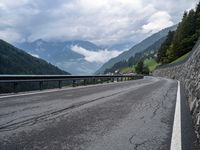 a road surrounded by mountains and tall trees with a cloudy sky above it below,