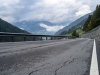 a road surrounded by mountains and tall trees with a cloudy sky above it below,