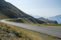 a motorcycle rides on the side of a winding road in the mountains overlooking a valley