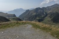 the mountain road winds through high altitude hills, the grass is grassy and green and there is a dirt pathway on either side of the hill