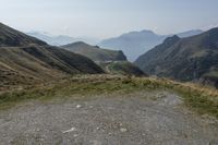 the mountain road winds through high altitude hills, the grass is grassy and green and there is a dirt pathway on either side of the hill