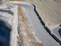 a motorcycle driving down a curve of the mountain road between two mountains, with a person riding on it