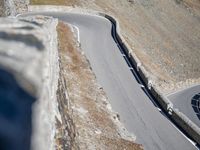 a motorcycle driving down a curve of the mountain road between two mountains, with a person riding on it