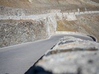 a man is on the side of a mountain road on his motorcycle by some stone wall