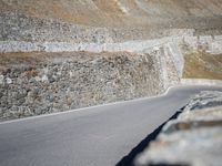 a man is on the side of a mountain road on his motorcycle by some stone wall