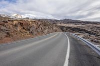 the side of a road next to mountains with snow capped peaks in the distance on a cloudy day