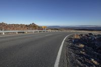 a sign on a curvy highway in the desert, with the view of a desert in the background