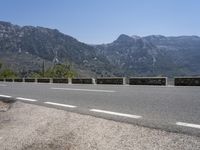 a long line of parked motorcycles next to the side of a mountain road, with the highway in front and on the other side of it with mountains