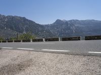 a long line of parked motorcycles next to the side of a mountain road, with the highway in front and on the other side of it with mountains