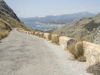 a view down a mountain road to the sea and mountains in the back ground with one motorcycle leaning up against the wall