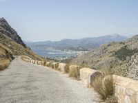 a view down a mountain road to the sea and mountains in the back ground with one motorcycle leaning up against the wall