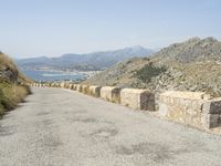 a view down a mountain road to the sea and mountains in the back ground with one motorcycle leaning up against the wall