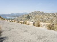 a view down a mountain road to the sea and mountains in the back ground with one motorcycle leaning up against the wall