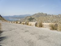 a view down a mountain road to the sea and mountains in the back ground with one motorcycle leaning up against the wall