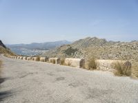 a view down a mountain road to the sea and mountains in the back ground with one motorcycle leaning up against the wall